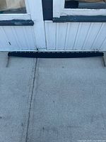 Full length of the old crosscut saw laid flat on concrete, showing its overall length and black coated blade.