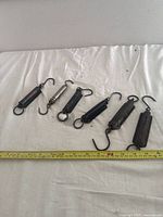 All six fish scale spring balances laid out horizontally on a white background with measuring tape above for size reference.