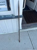 Old metal pinch bar leaning against a white wooden wall on concrete floor, showing full length.