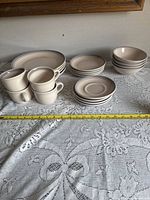 Photo showing stacks of dinner plates, side plates, bowls, and cups arranged on a lace cloth with measuring tape for scale.