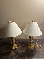 Two table lamps with beige fabric conical shades and beige distressed bases on a worn surface