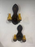 Pair of vintage amber glass wall sconces mounted on pegboard, showing front view with ornate metal backplates and two amber glass shades per sconce.