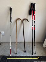 Full view of four walking sticks and canes arranged against a wall with measuring tape on the ground