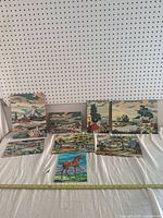 All seven paint by numbers art pieces arranged on white fabric, showing landscapes and horse. Paintings appear painted with muted natural colors with some wear visible.