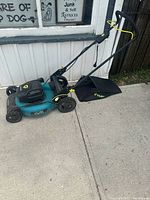 Electric Yardworks lawn mower positioned outside on a concrete surface near a building. Showing the left side profile including handlebar and collection bag.