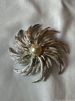 Front view of silver-tone sunburst brooch with faux pearl centre