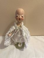 Front view of porcelain doll on stand showing dress and missing wig