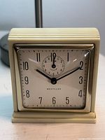 Front view of square ivory Westclox wind-up alarm clock showing dial and hands