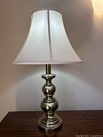 Full front view of the 27 inch brass lamp with ivory shade on a wooden table against a light wall.