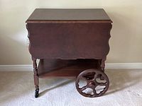 Front view of the antique style tea and bar cart showing the main body, drop leaf side, and removable decorative wooden wheel.