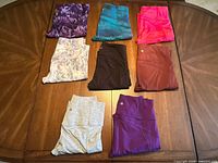 Eight pairs of folded women’s small Athleta leggings in various colors and patterns laid out on a wooden table