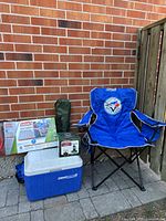 Lot contents showing Coleman cooler, camping stove box, air mattress box, and Blue Jays branded camping chair.