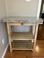 Front view of butcher's block showing speckled stone top, wooden drawer, and two slatted shelves