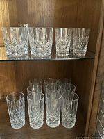 Shelf display of two types of crystal drinking glasses, tall and short with detailed cut patterns.