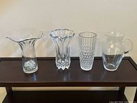 Front view of lot showing all 4 vases with varying shapes and clear transparency on dark wooden table