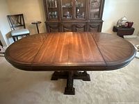 Front angle view of the vintage solid wood dining table with both leaves inserted showing the full extended oval tabletop and pedestal base.
