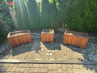 Photo of 3 wooden garden planters, 2 large rectangular and 1 smaller square, arranged outdoors on stone patio with soil inside.