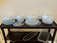 Overview of glass dishes on wooden table, showing leaf pattern plates, bowls, geometric plates and bowls, and glass bakeware below