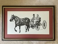 Clear photo of the framed black and white print showing two men seated in a horse drawn buggy, signature and date visible on print.
