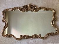 Front view of ornate gold painted plaster frame hanging mirror on carpet background.