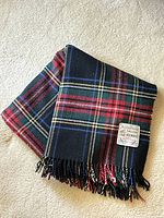Folded Highland Home Scottish Wool Blanket laid on carpet. Shows color and fringed edges.
