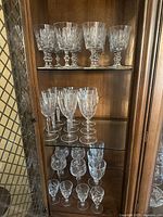 Front view of entire cabinet showing all crystal wine glasses arranged by size on three glass shelves, illustrating variety and condition.