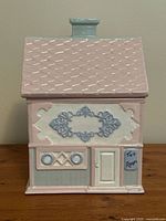 Front view of ceramic tea canister shaped like a pink and blue tea room building with signage.