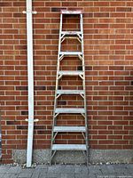 Full frontal image of the 8 ft aluminum ladder against a brick wall, showing seven steps and the overall structure supporting it upright.