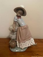 Full view of the Lladro porcelain figurine showing the girl leaning against the stone wall with the jug at the base.