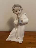 Full view of porcelain angel playing flute figurine on wooden surface against beige background.