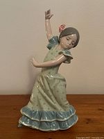 Front view of the Lladro Lolita Flamenco dancer figurine showing the figure in mid-dance with right arm raised and left arm horizontally extended, wearing a pale grey dress with blue polka dots and blue ruffle hem, hair tied back with flower detail.