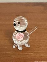 Front view of miniature clear crystal dog figurine, showing detailed faceted head and body, black eyes and nose, black collar, and pink flower decoration on chest.