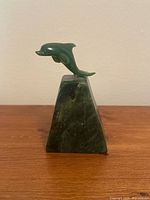 Front angled view of a green nephrite jade dolphin mounted on a polished dark green nephrite jade stone base with natural variations.