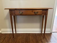 Front view of pine console table showing narrowed rectangular shape, tapered legs, and false drawer with brass handles.