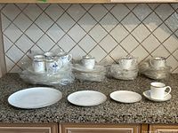 Full view of stacks of dishes in original plastic behind one of each piece unwrapped on countertop.
