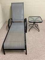 Side angle of metal reclining patio lounger and glass top table showing overall condition and details