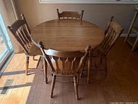 Round pine dining table with 4 spindle back chairs and 1 armchair, shown in natural light on hardwood floor.