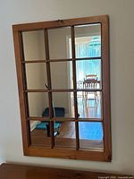 Front view of vintage pine framed mirror with grid design, showing reflections of interior space including a dining room table and chair.