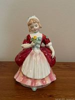Front view of Royal Doulton porcelain figurine of a girl in red dress holding a yellow rose. The figurine has detailed facial features and bright glaze finish.
