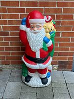Front view of plastic Santa Claus lawn decoration against brick wall.