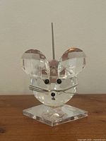 Front view of clear faceted crystal mouse figurine with metal whiskers, black eyes and nose, mounted on a clear crystal base, with metal spring coil tail extending upward.