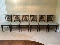 Front-facing view of six vintage dining chairs in a row, five side chairs and one armchair with arms, showing the distinctive Y-shaped backrests and upholstered light fabric seats.