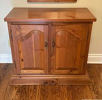 Front view of vintage handmade pine cabinet showing wood grain, two doors with brass handles, and a base molding