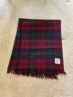 Folded wool tartan blanket showing pattern and fringed edges on beige background.