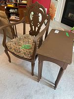 Photo of brown wooden accent chair with floral seat cushion and one nesting table beside it on carpeted floor