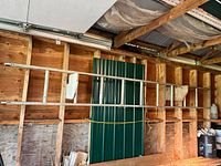 Aluminum extension ladder seen horizontally mounted on wall inside wooden shed, showing full length and structure.