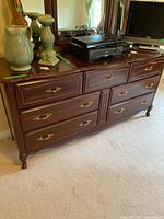 Front view of wooden dresser showing seven drawers with brass handles and polished wood grain finish.