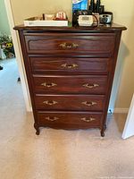 Front view showing the 5 drawers with ornate brass handles and decorative carved details on drawer fronts and legs.