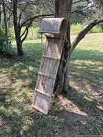 Antique wooden toboggan leaning against a tree outdoors, showing the curved wooden front and vertical slats of the toboggan.