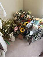 Full view of the corner with multiple bunches of artificial flowers and some decor on a metal stand including candles and figurines